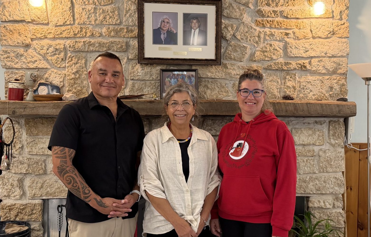 Wayne Monague, Maggie Dieter and Kristi Degenhardt stand together as new Ministry Formation Team, in front of fireplace, under photos of school namesakes Dr. Jessie Saulteaux and Francis Sandy.